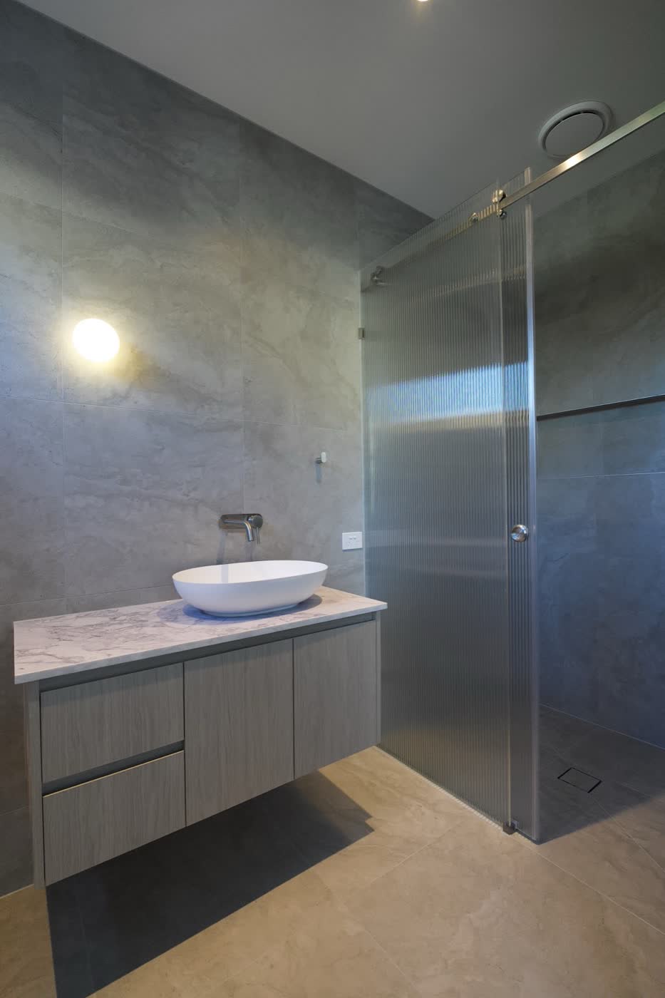 A main bathroom in one of Manraj Nijjar's own builds, a rectangular room with a floating vanity, stone benchtop and a fluted glass shower screen