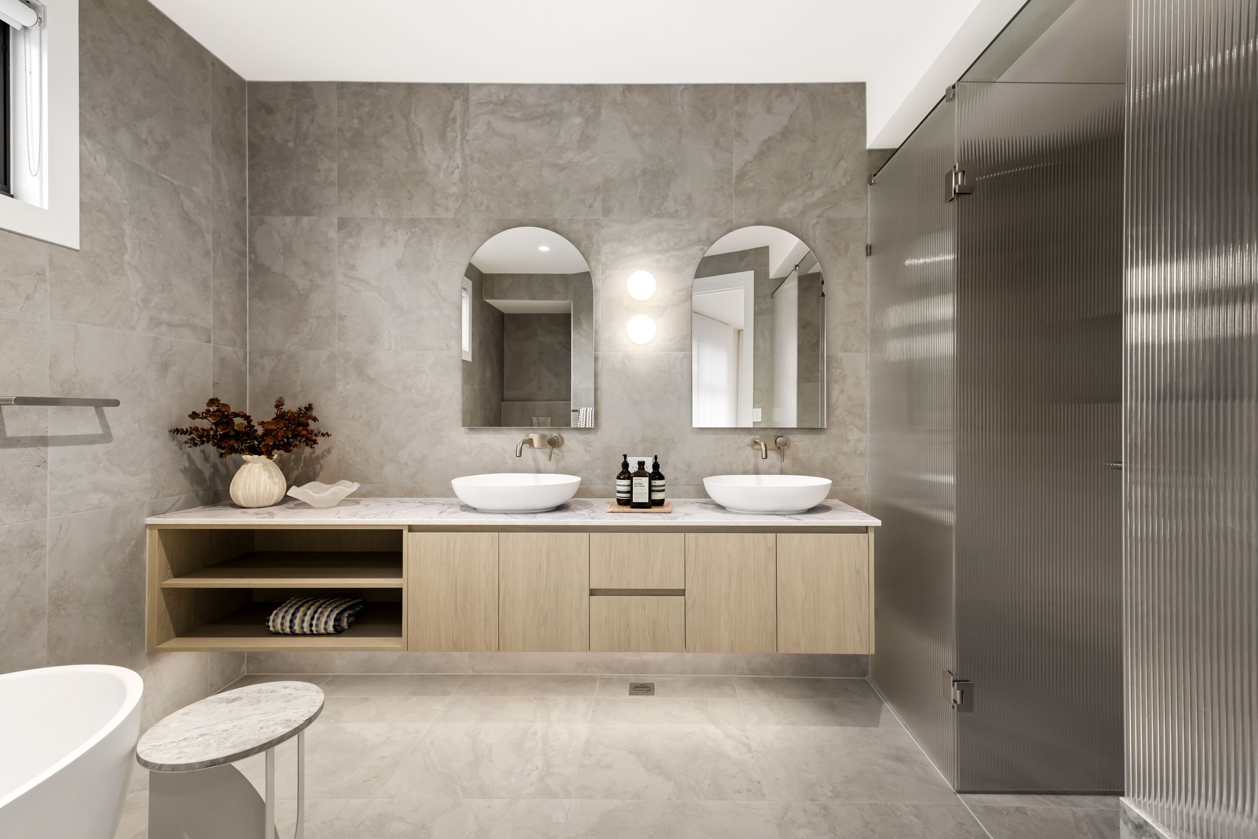 The master ensuite at Renshaw, Manraj Nijjar's own house: twin arched mirrors, wall mounted tapware, a stone benchtop on oak joinery and a fluted glass shower screen